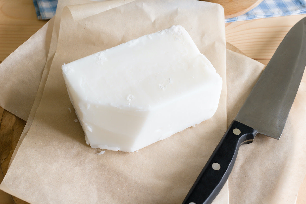 Block of grass fed tallow on brown parchment paper with a knife next to it on a kitchen table